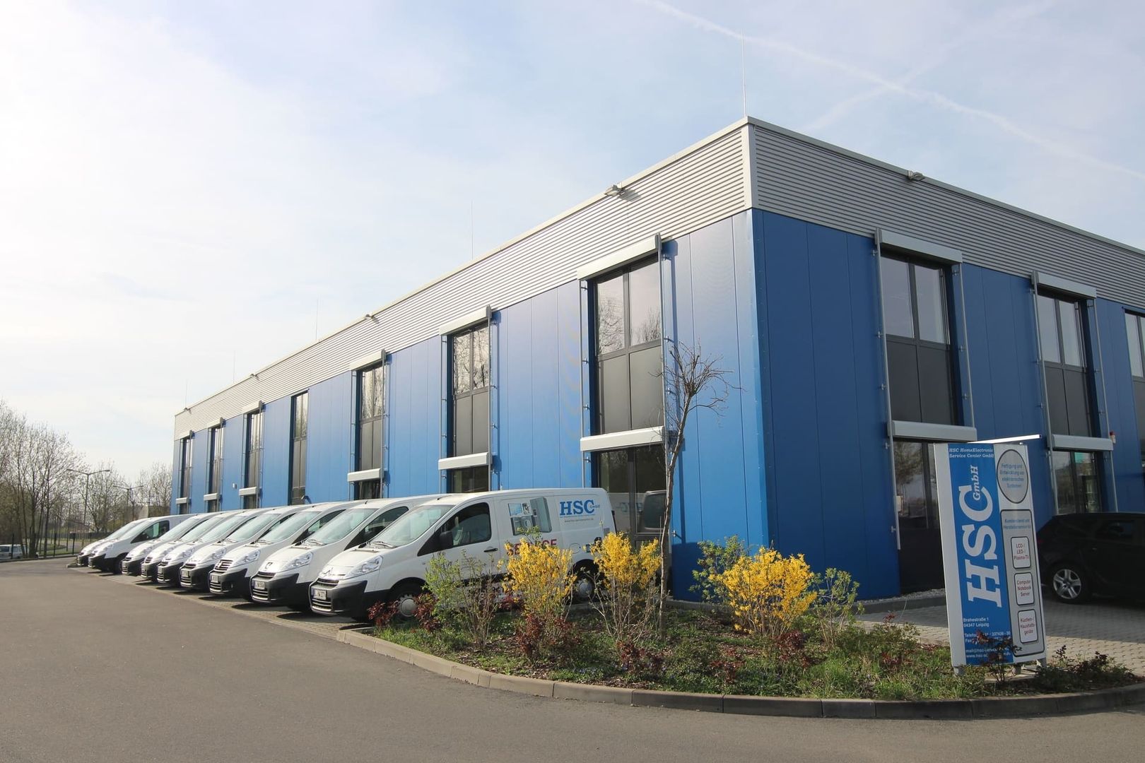 Eine Gruppe weißer Firmentransporter parkt vor dem Unternehmensgebäude