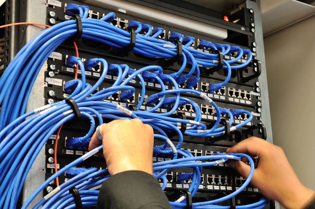 Techniker beim Verlegen von Netzwerkkabeln in einem Serverschrank professionelle IT Installation
